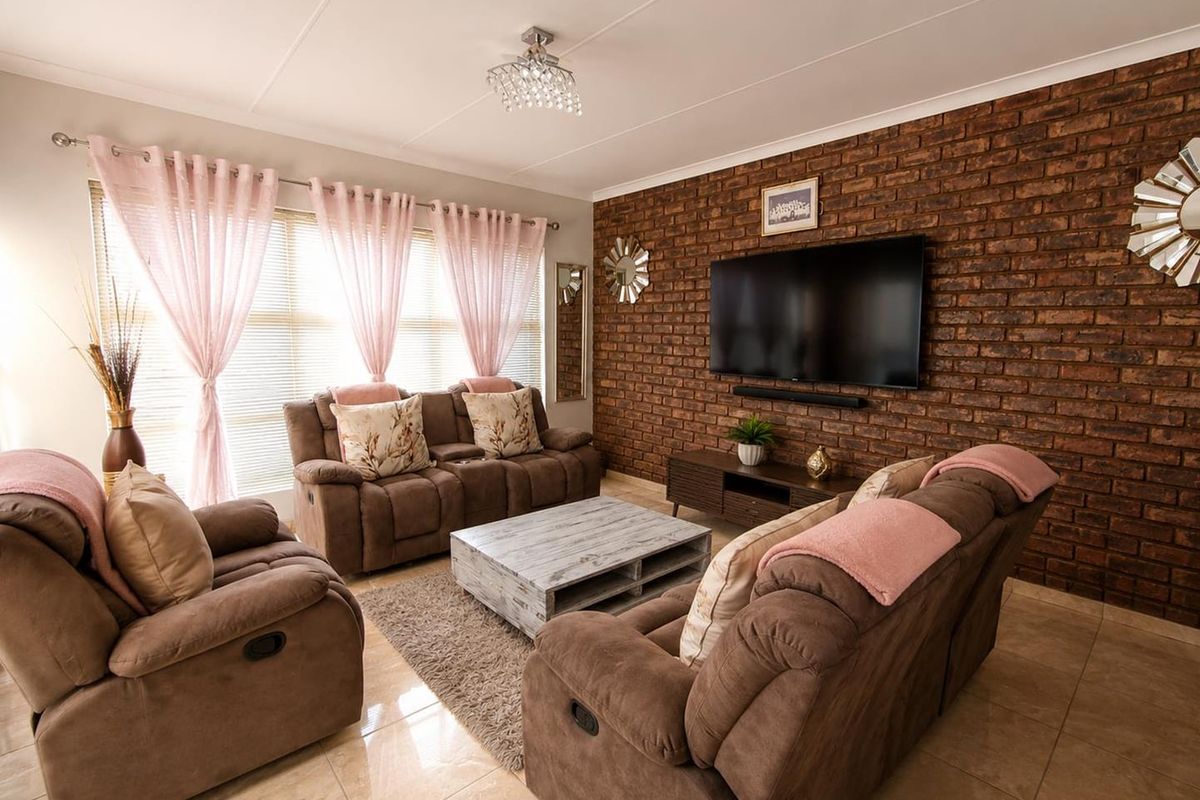 A well-maintained living room featuring a prominent exposed brick feature wall, polished tile flooring, and elegant crystal lighting.