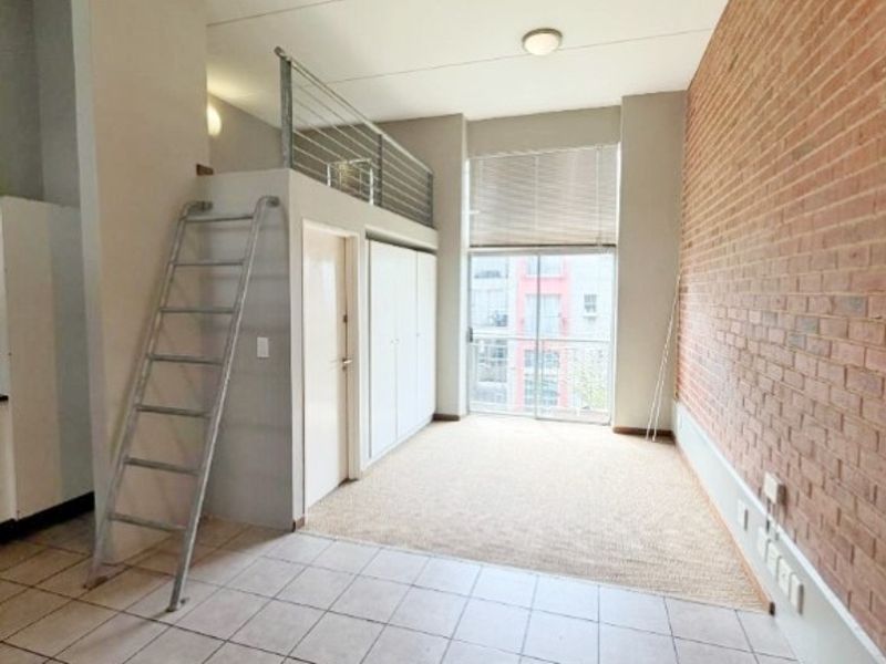 Open plan living area featuring an exposed brick wall, tiled flooring, and a mezzanine level accessible via a metal ladder.