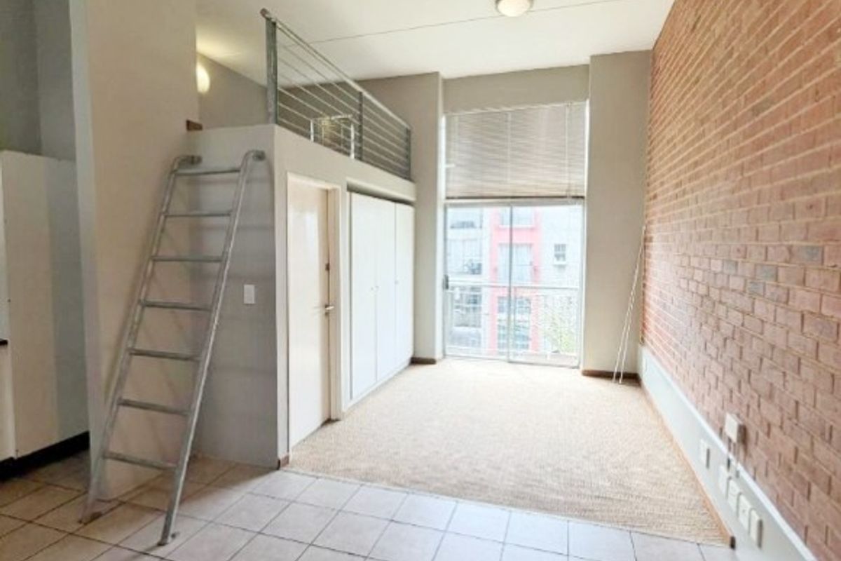 Open plan living area featuring an exposed brick wall, tiled flooring, and a mezzanine level accessible via a metal ladder.