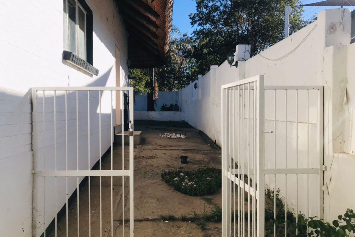 A narrow rear courtyard area featuring a thatched roof overhang, concrete paving, and a white perimeter wall with security gate access.