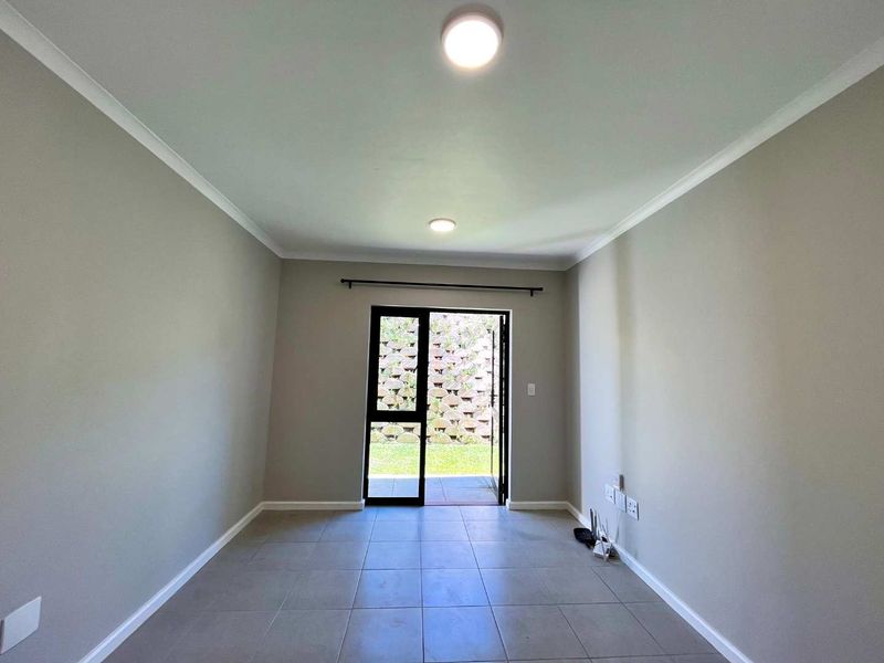 A bright, empty living room featuring neutral tiled flooring, recessed lighting, and a sliding glass door providing direct access to the outdoor area.