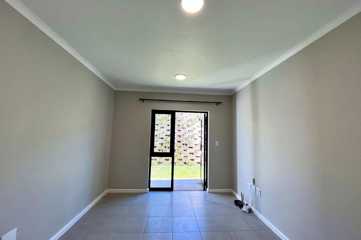 A bright, empty living room featuring neutral tiled flooring, recessed lighting, and a sliding glass door providing direct access to the outdoor area.