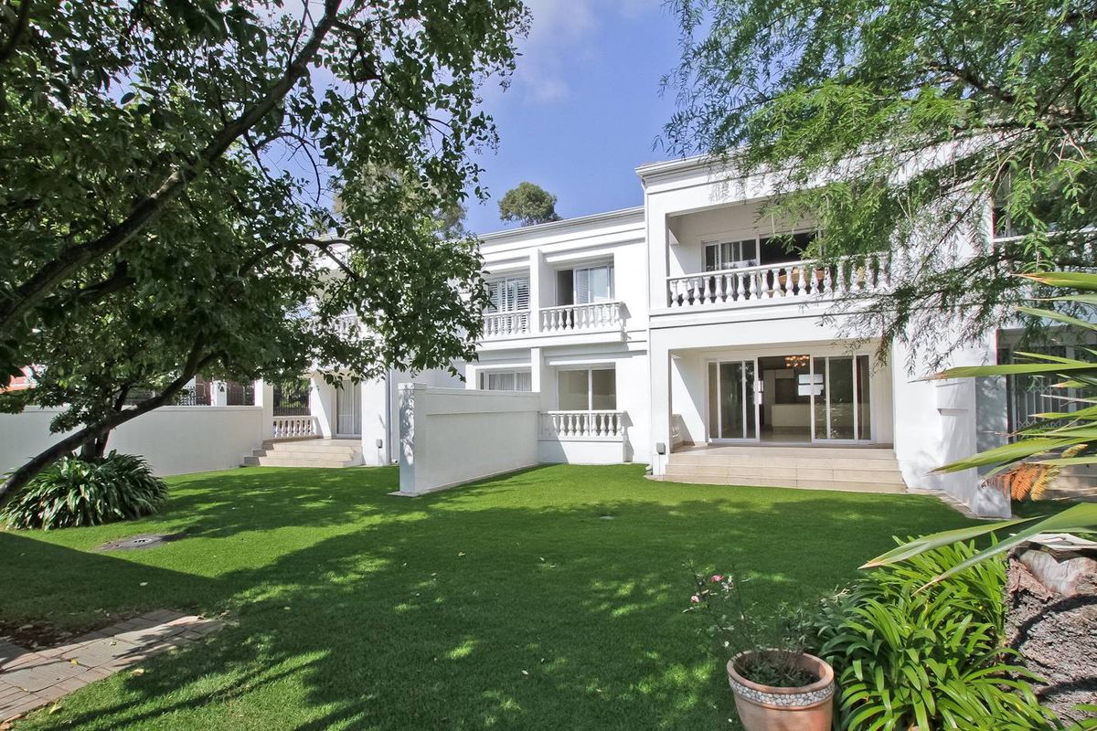 Rear view of the townhouse featuring a well-maintained lawn, paved patio areas, and upper-level balconies with classic balustrades.