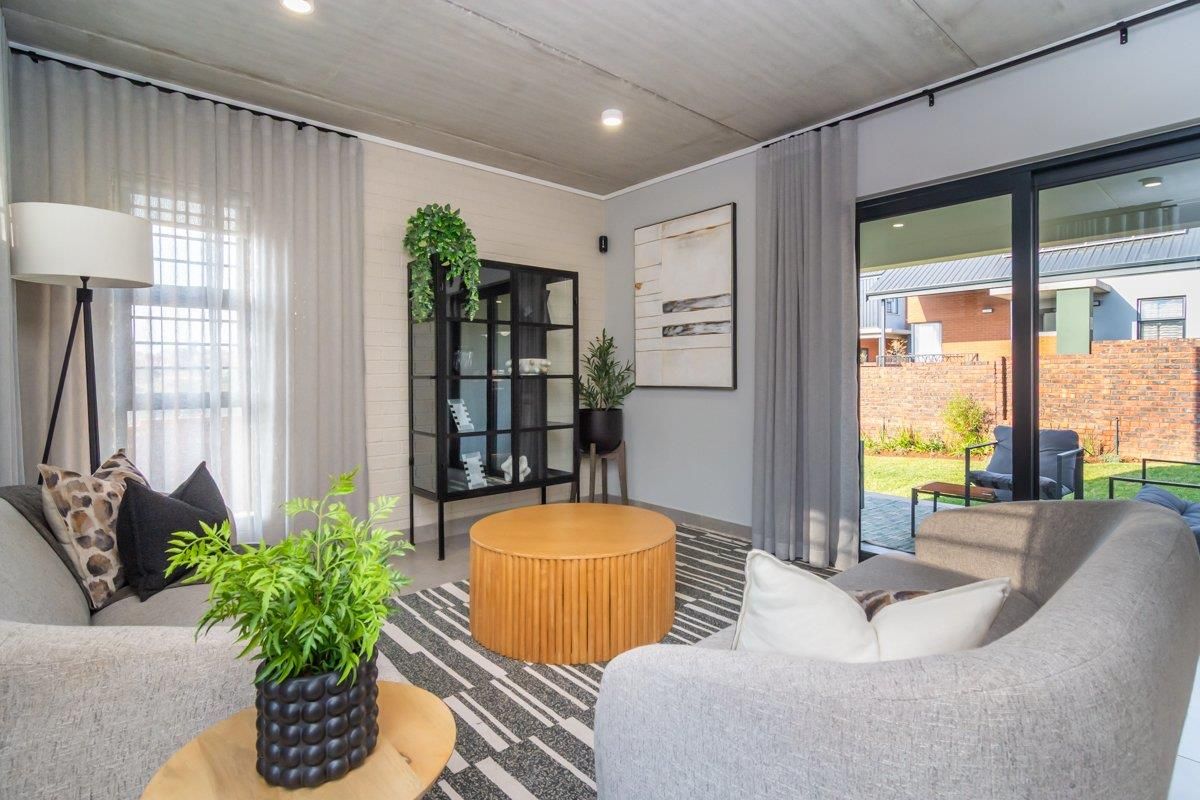 Modern living room featuring an exposed concrete ceiling, painted brick accent wall, and large sliding glass doors providing seamless access to the rear garden.