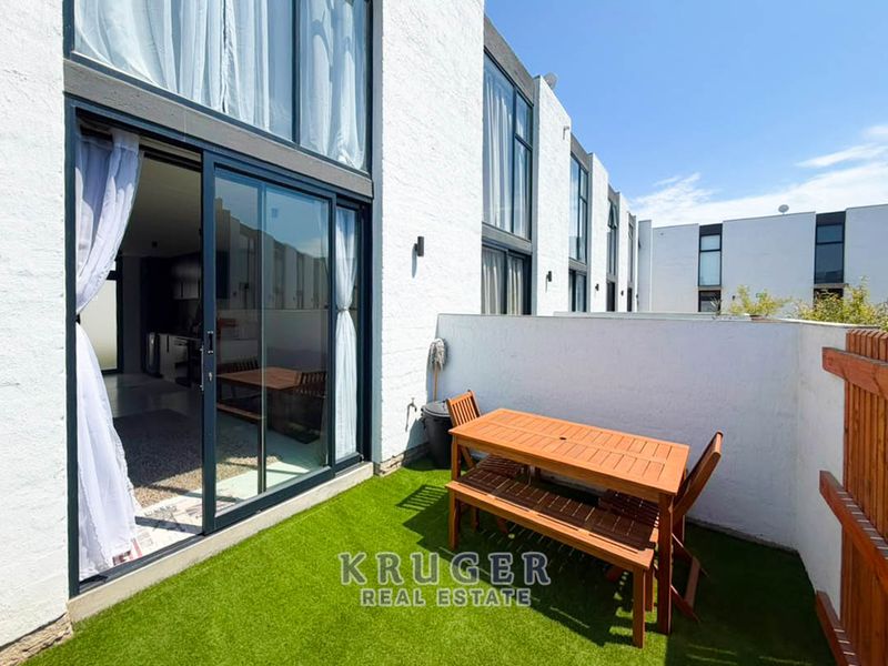 A modern ground-floor patio featuring artificial turf, sliding glass doors providing indoor-outdoor flow, and exterior wall lighting.