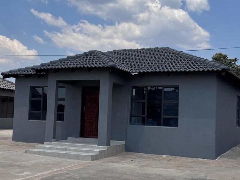 A modern, well-maintained townhouse exterior featuring a dark grey facade, tiled roof, and a paved driveway entrance.