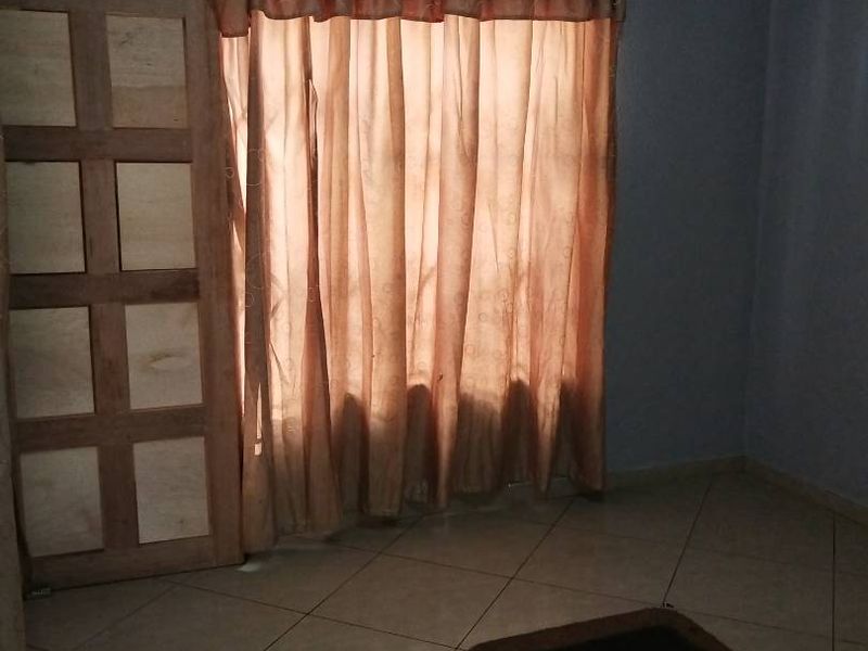 An empty living room featuring tiled flooring and a wooden panel door, providing a blank canvas for potential interior design updates.
