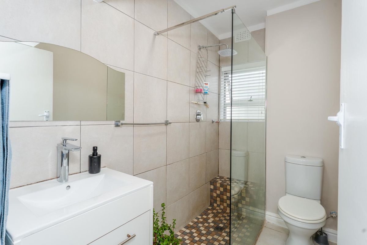 Modern bathroom featuring a walk-in shower with glass screen, mosaic tiled shower floor, wall-mounted vanity, and a standard toilet.
