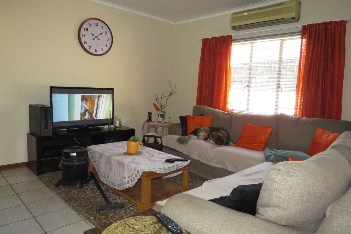 A comfortable living room featuring tiled flooring, a wall-mounted air conditioning unit, and a large window with curtains.