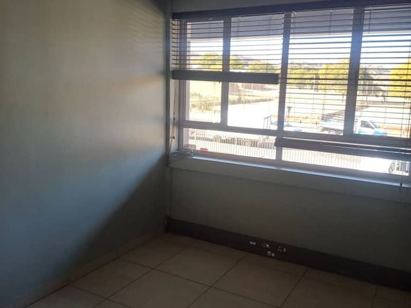 A vacant office space featuring tiled flooring, a suspended ceiling with recessed lighting, and large windows fitted with venetian blinds.
