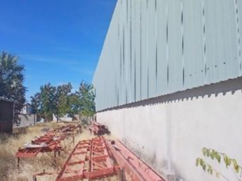 Rear exterior view of the industrial property featuring corrugated metal cladding and a concrete foundation wall with surrounding overgrown grounds.