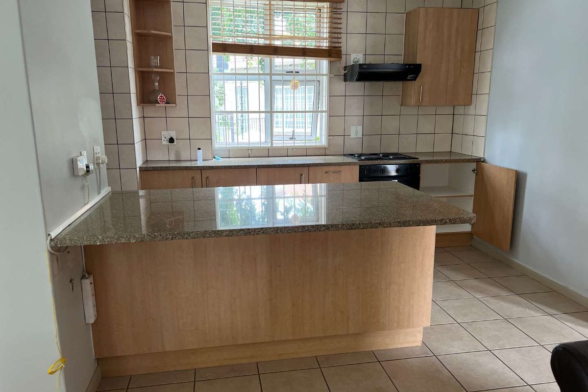 A functional kitchen featuring granite countertops, built-in oven, hob, extractor fan, and tiled finishes, offering a practical layout for daily meal preparation.