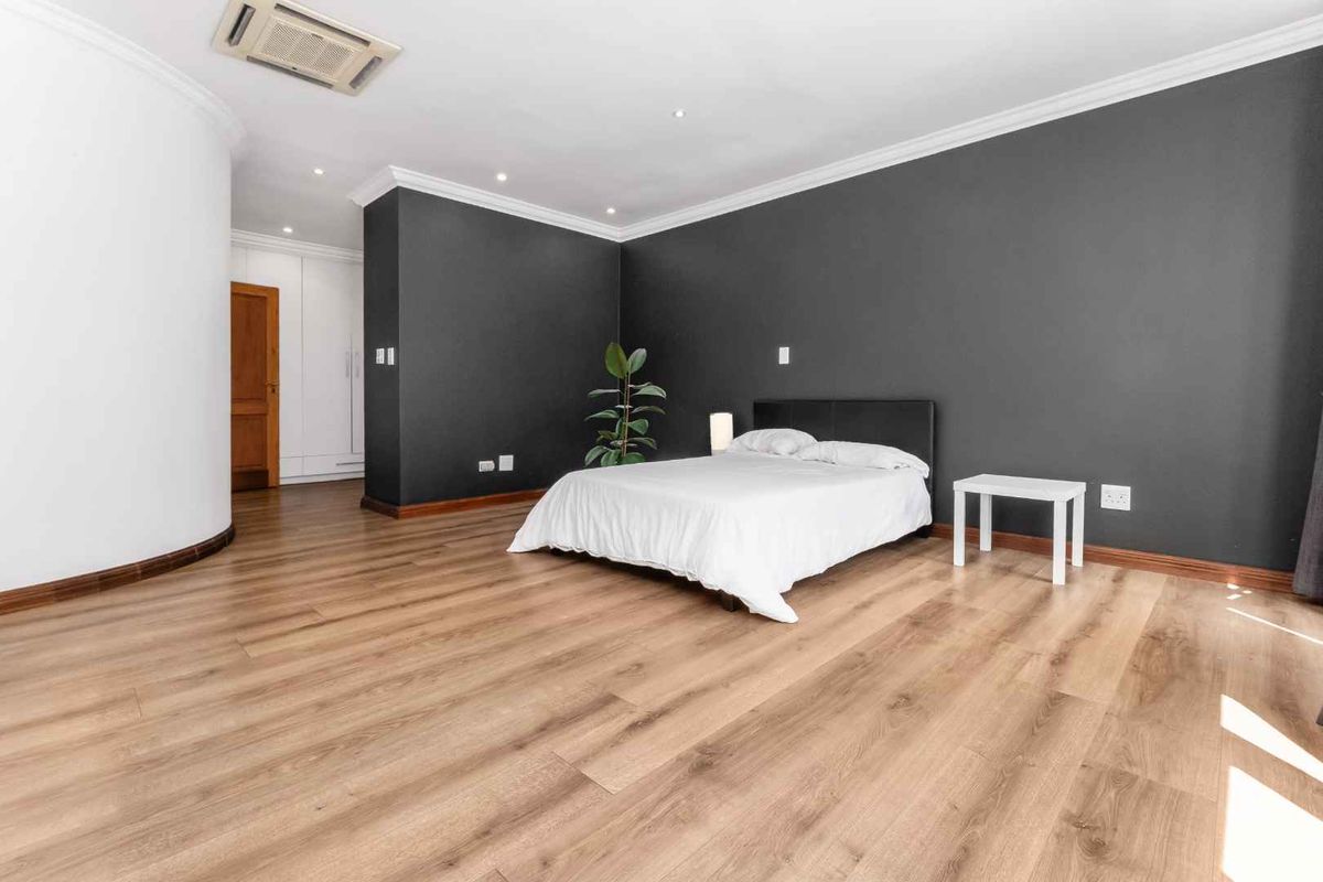 Spacious bedroom featuring modern laminate flooring, dark accent wall, built-in cupboards, and integrated ducted air conditioning.