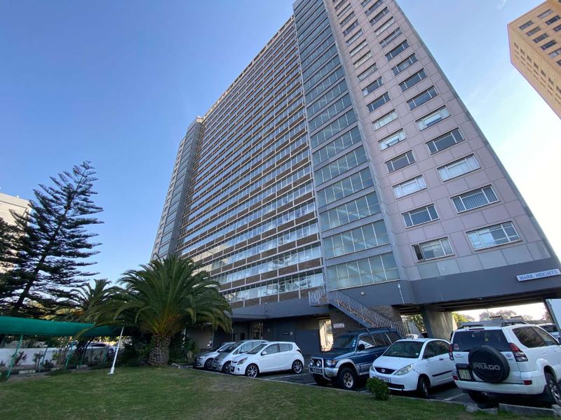 A low-angle view of the Mark Heights apartment building exterior, featuring a multi-story facade, ground-level parking area, and landscaped front lawn.