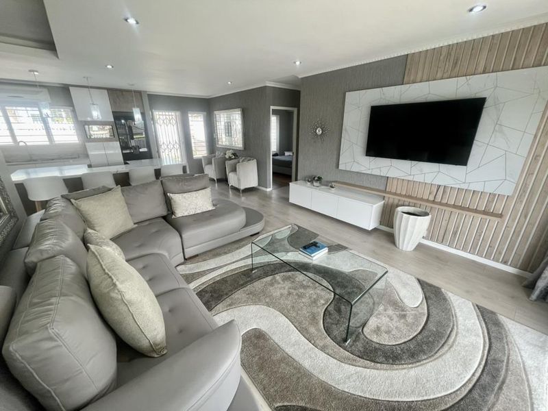 Spacious open-plan living area featuring modern laminate flooring, recessed lighting, and a contemporary feature wall with integrated media space and kitchen island.