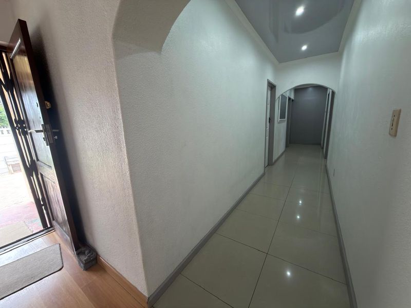 A clean, well-lit hallway featuring tiled flooring, arched architectural details, and recessed ceiling lights, providing a bright transition between living spaces.