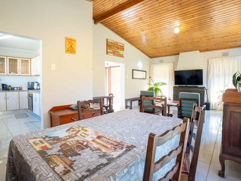 Open-plan living and dining area featuring a timber-clad vaulted ceiling, tiled flooring, and a built-in fireplace, with an adjoining kitchen.