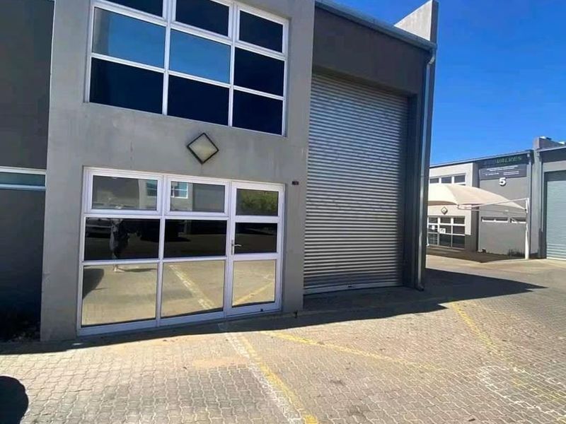 Front elevation of a commercial unit featuring a large roller shutter door, glass entrance, and paved driveway access.