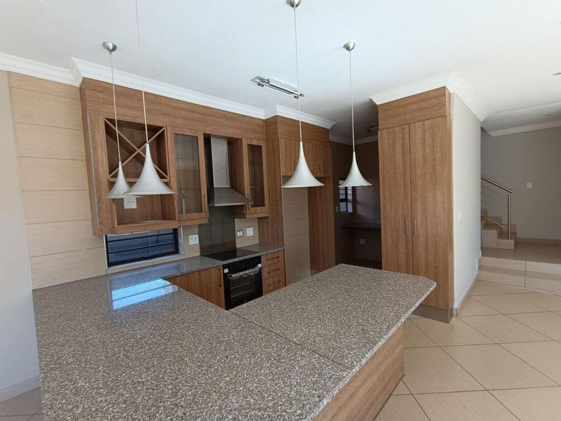 Modern kitchen featuring granite countertops, built-in oven with extractor fan, wooden cabinetry, and a breakfast bar, finished with neutral floor tiles.
