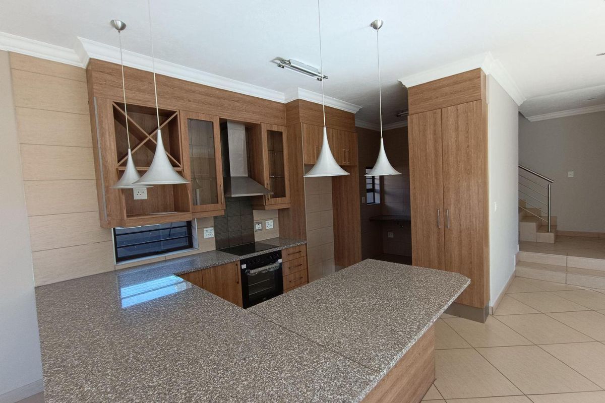 Modern kitchen featuring granite countertops, built-in oven with extractor fan, wooden cabinetry, and a breakfast bar, finished with neutral floor tiles.