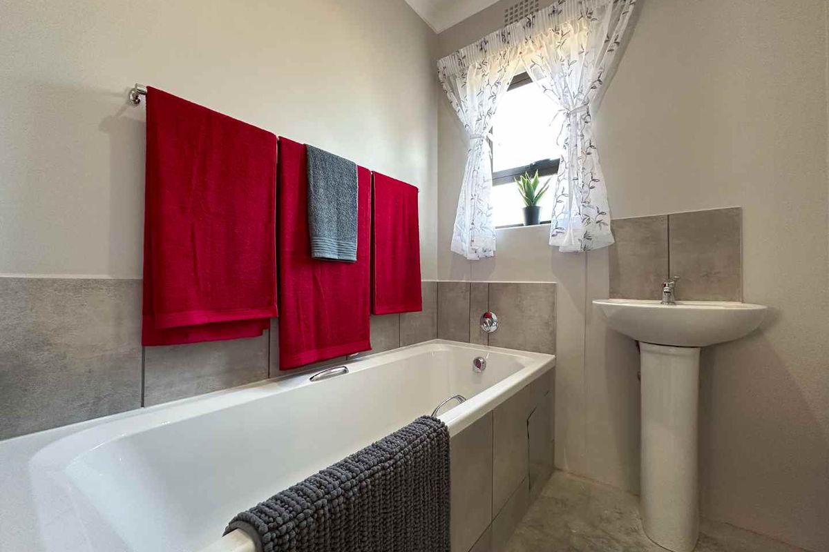 A functional bathroom featuring a white bathtub with tiled surround and a pedestal sink, finished with neutral wall tones.
