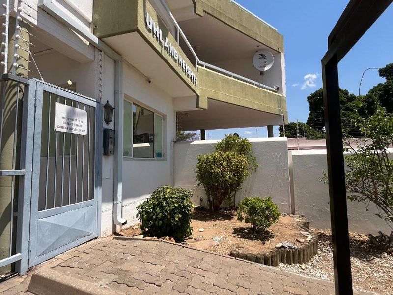 Exterior view of the apartment building entrance featuring a security gate, electric fencing, and paved access area.