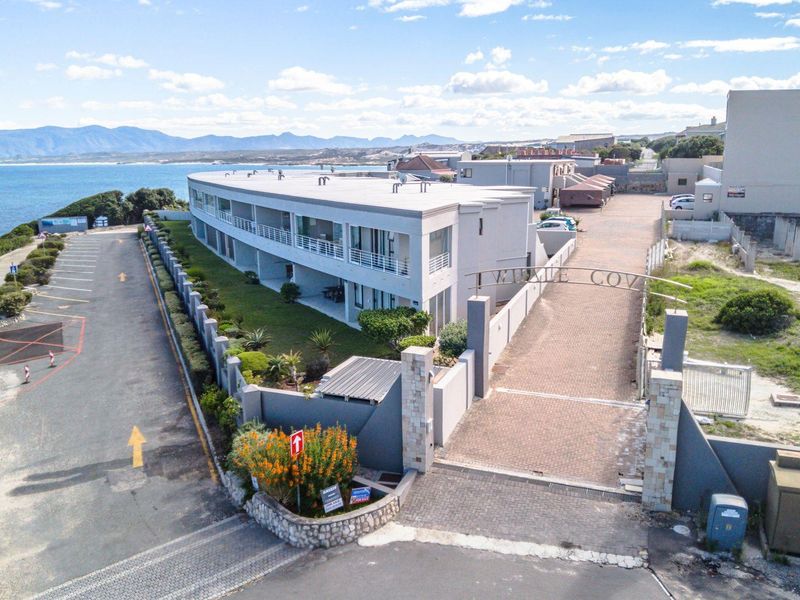 Aerial view of the apartment complex entrance, featuring a gated driveway, landscaped grounds, and coastal proximity.
