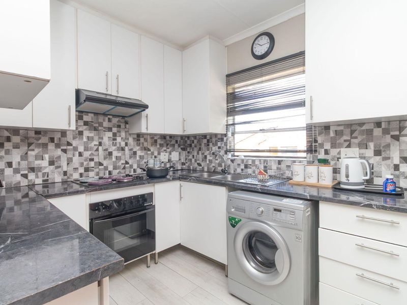 A functional kitchen featuring white cabinetry, dark laminate countertops, a tiled mosaic backsplash, and integrated appliances including an oven and extractor fan.
