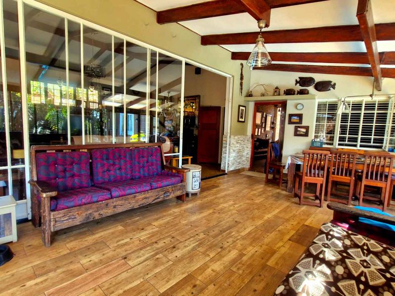 Spacious covered patio featuring exposed timber beams, wood-look tile flooring, and large glass sliding doors connecting to the interior living space.