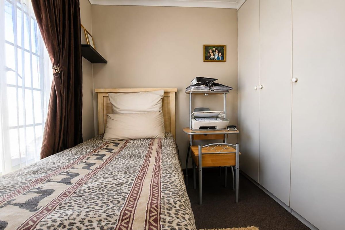 A functional bedroom featuring built-in cupboards and carpeted flooring, offering a practical space with natural light from the window.