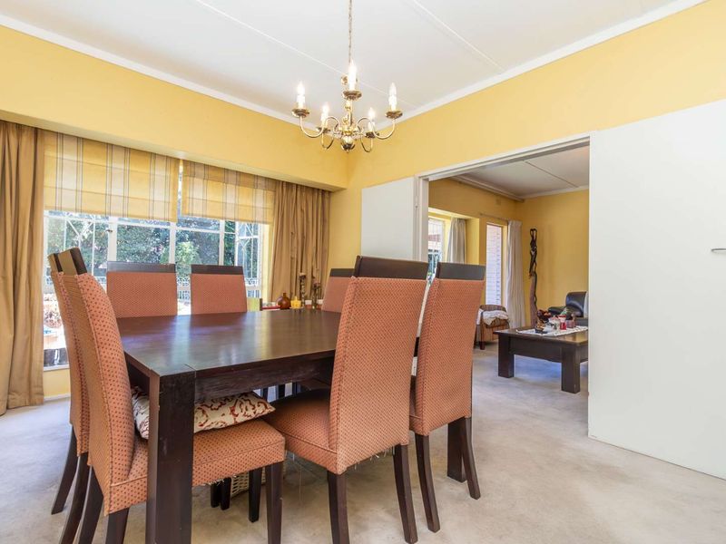 A bright dining room featuring a classic chandelier, large windows, and direct access to the adjacent living area through double doors.