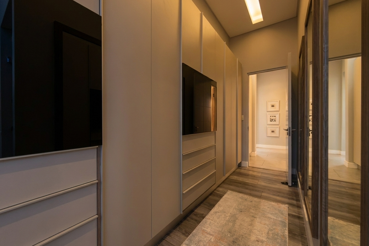 A modern walk-in closet featuring floor-to-ceiling built-in cabinetry, integrated shelving, and full-length mirrored doors, finished with high-quality wood-look flooring and recessed lighting.