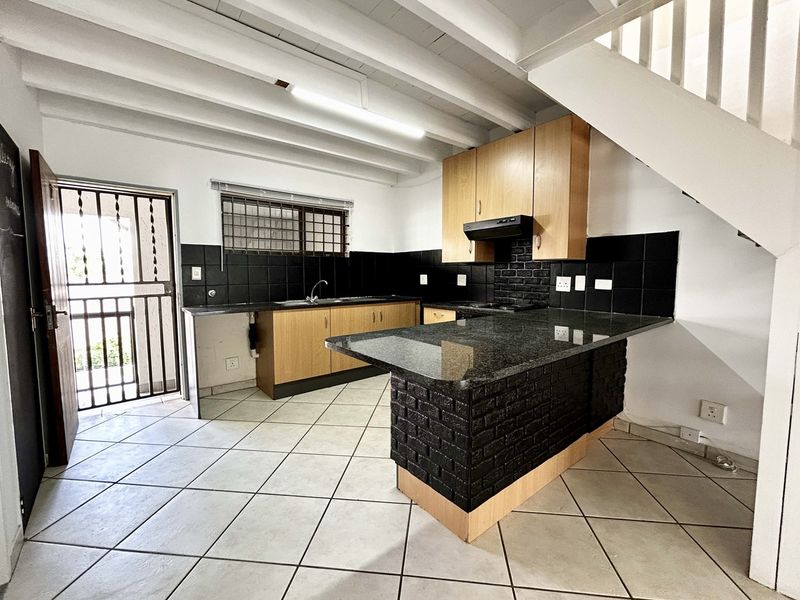 A functional kitchen featuring granite countertops, a brick-faced breakfast bar, built-in cabinetry, and tiled flooring, situated beneath an open staircase.