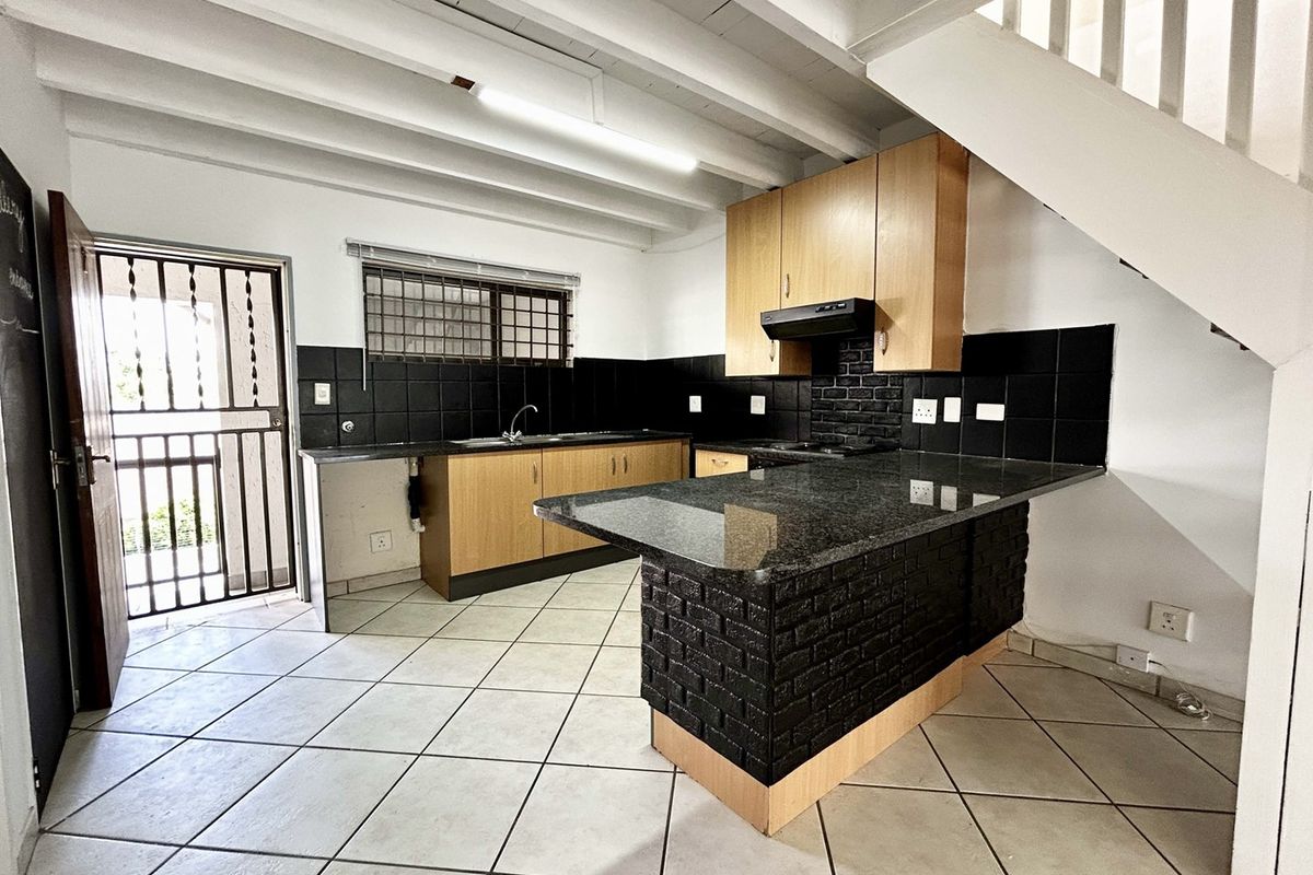 A functional kitchen featuring granite countertops, a brick-faced breakfast bar, built-in cabinetry, and tiled flooring, situated beneath an open staircase.