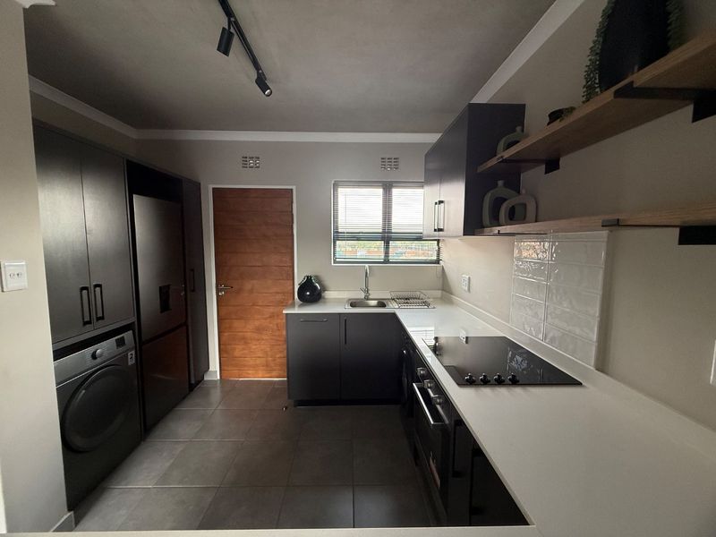 Modern kitchen featuring dark cabinetry, white countertops, integrated appliances, subway tile backsplash, and sleek track lighting in a well-maintained, contemporary space.