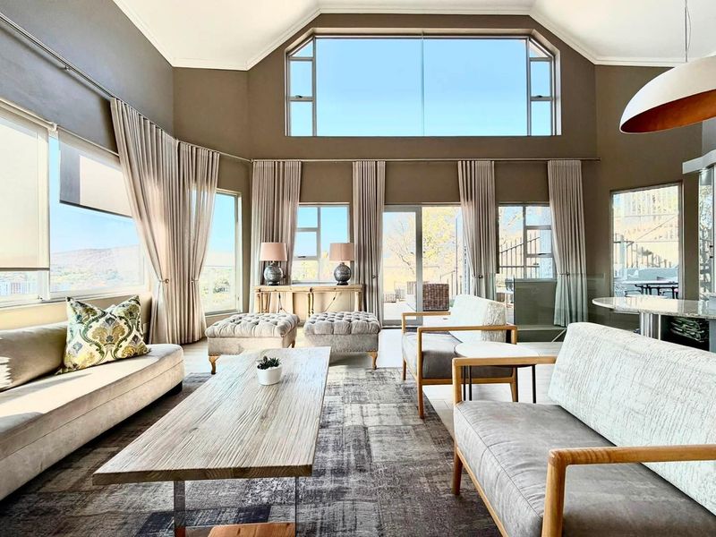 Spacious living room featuring a high vaulted ceiling, expansive windows providing natural light, and direct access to an outdoor patio area.