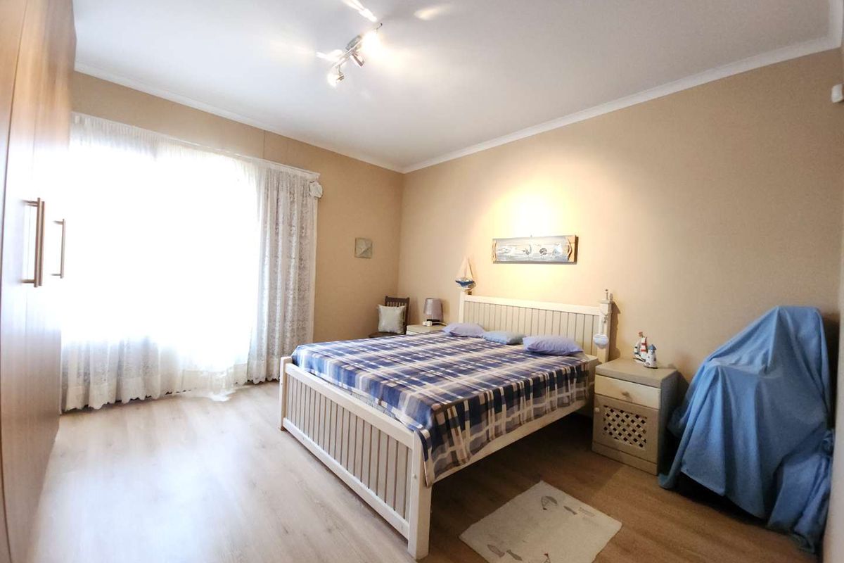 A spacious bedroom featuring light wood-look flooring, built-in wardrobes, and a large window with curtains, offering a neutral and functional living space.
