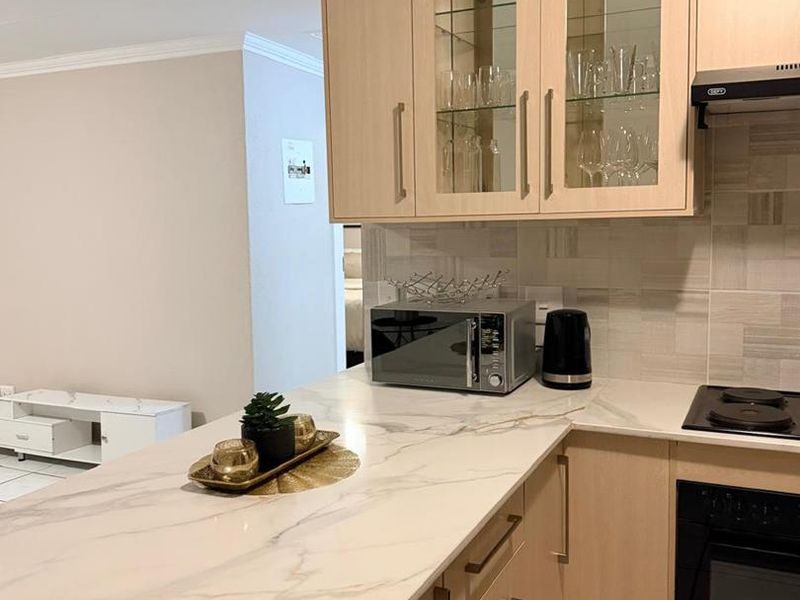Modern kitchen featuring light wood cabinetry, marble-look countertops, built-in oven, electric hob, and a stylish tiled backsplash.