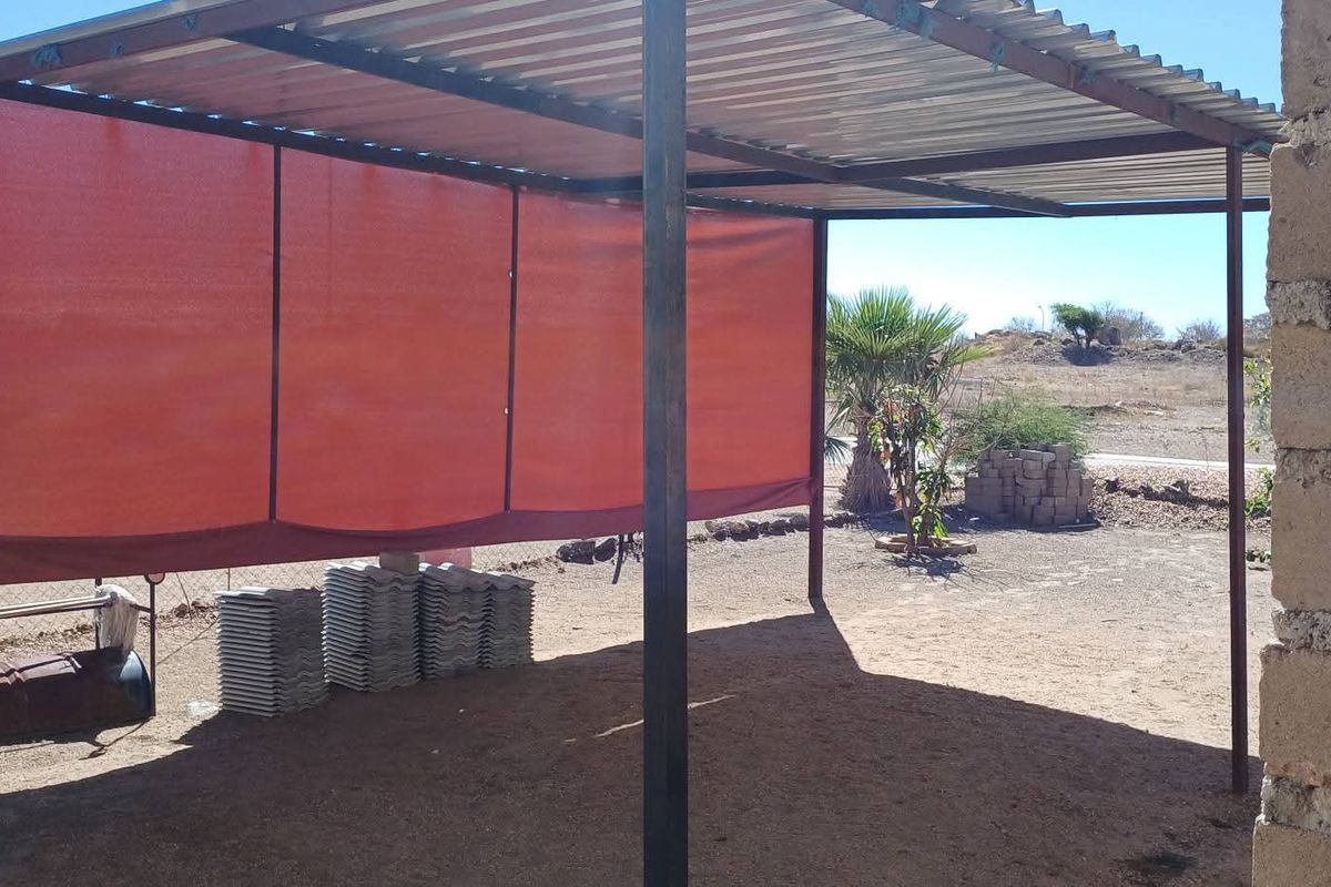 A simple outdoor covered patio area featuring a corrugated metal roof supported by metal posts and a privacy shade screen.