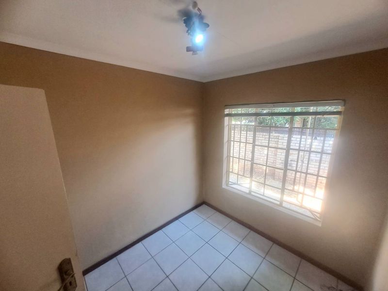 An empty bedroom featuring tiled flooring, security bars on the window, and neutral wall paint, ready for personalization.