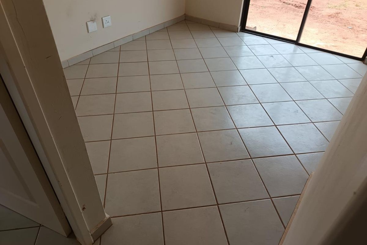 An empty room featuring neutral ceramic floor tiles, sliding glass doors leading to the exterior, and standard electrical wall outlets.