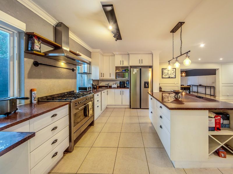 Spacious kitchen featuring granite countertops, a large central island, gas stove with extractor, and ample built-in cabinetry with modern lighting.