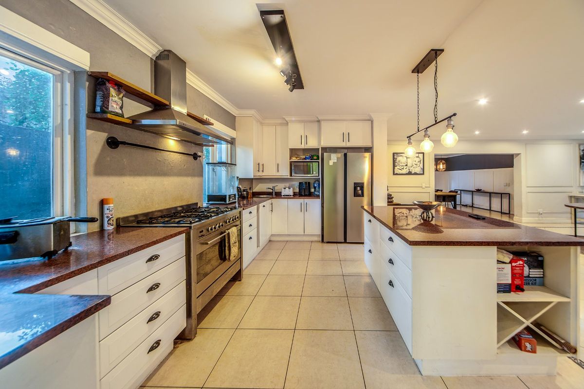 Spacious kitchen featuring granite countertops, a large central island, gas stove with extractor, and ample built-in cabinetry with modern lighting.
