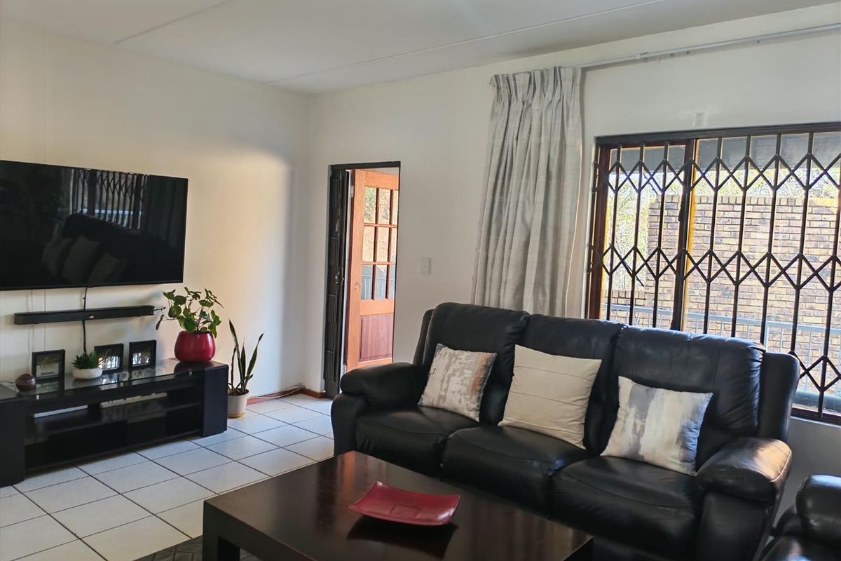 A living room featuring tiled flooring and a sliding door with security gate, providing access to the exterior.