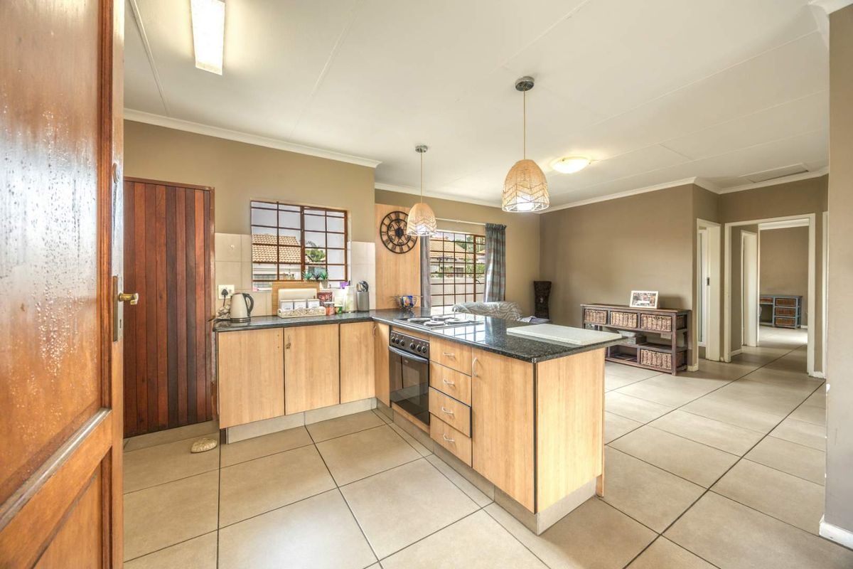 Open-plan kitchen featuring light wood cabinetry, granite countertops, built-in oven, and hob, seamlessly flowing into the living area with neutral tiled flooring.