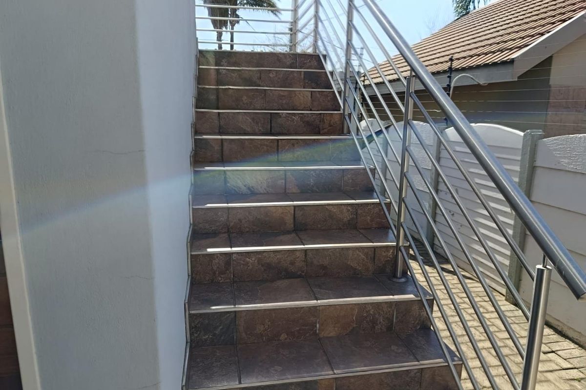 Exterior staircase featuring tiled steps and a modern stainless steel balustrade leading to an upper level.