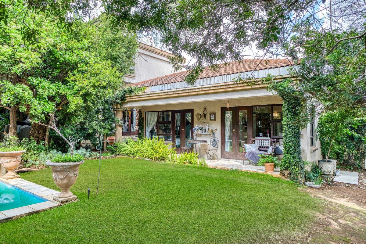 A charming rear exterior view featuring a landscaped garden, a swimming pool, and a covered patio with access through multiple sets of french doors.