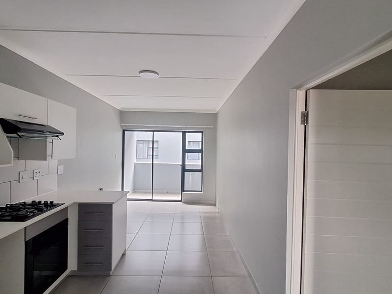 Modern open-plan kitchen and living area featuring tiled floors, built-in cabinetry with gas hob and oven, leading to a private balcony.