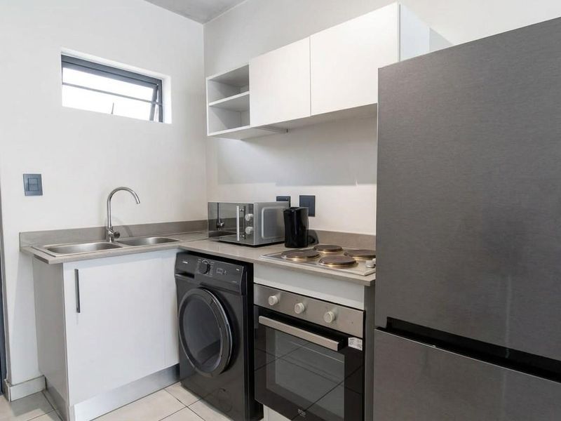 Compact modern kitchen featuring white cabinetry, stone countertops, integrated electric hob and oven, stainless steel sink, and tiled flooring.