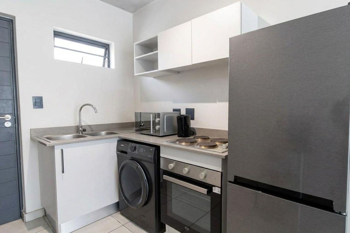 Compact modern kitchen featuring white cabinetry, stone countertops, integrated electric hob and oven, stainless steel sink, and tiled flooring.
